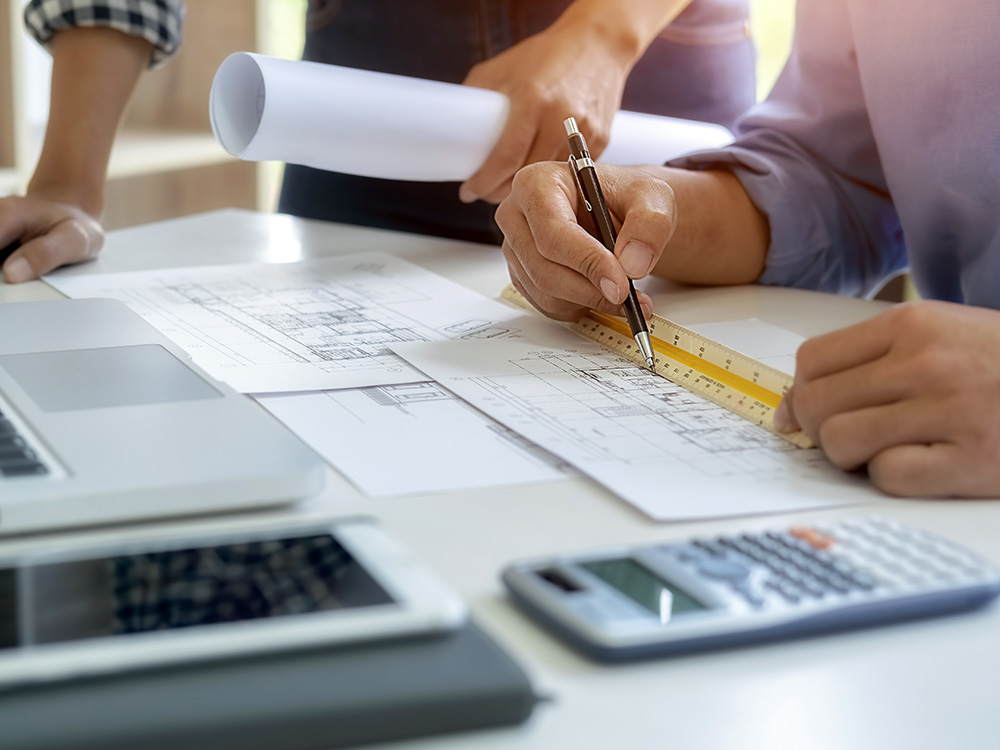 H&auml;nde mit Stift und Lineal &uuml;ber Baupl&auml;nen am Schreibtisch mit Laptop und Taschenrechner